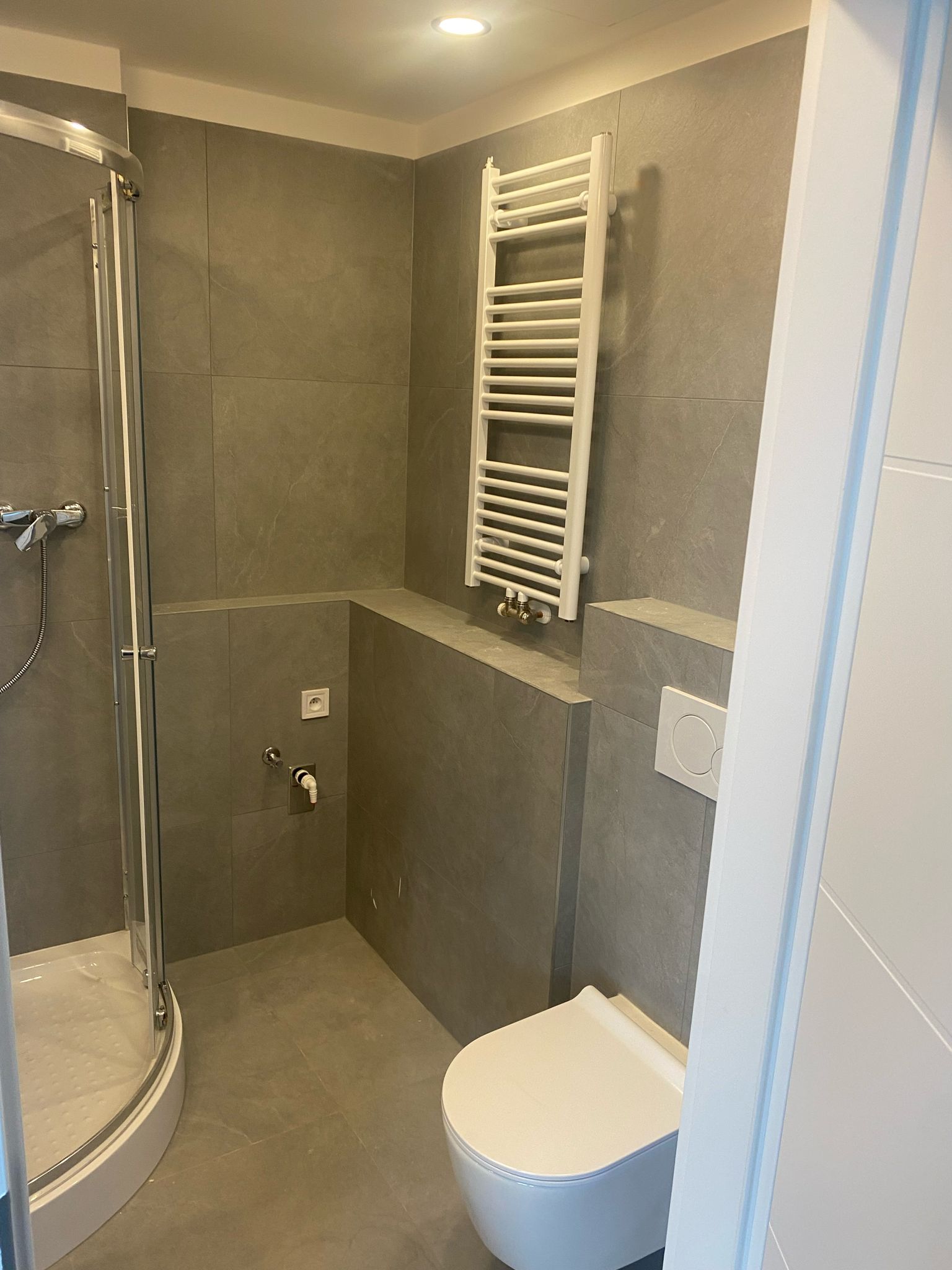 Čtvrtkruhový sprchový kout, závěsné WC a bílý žebříkový radiátor